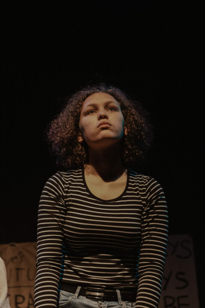 young girl with curcly hair and stripy top looking up into a theatre light