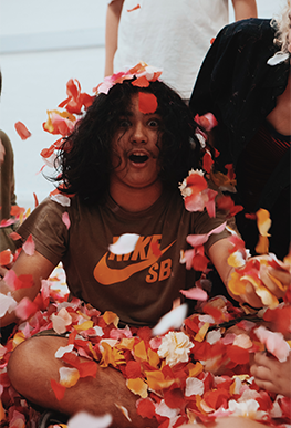 A boy with long hair is showered in flower petals
