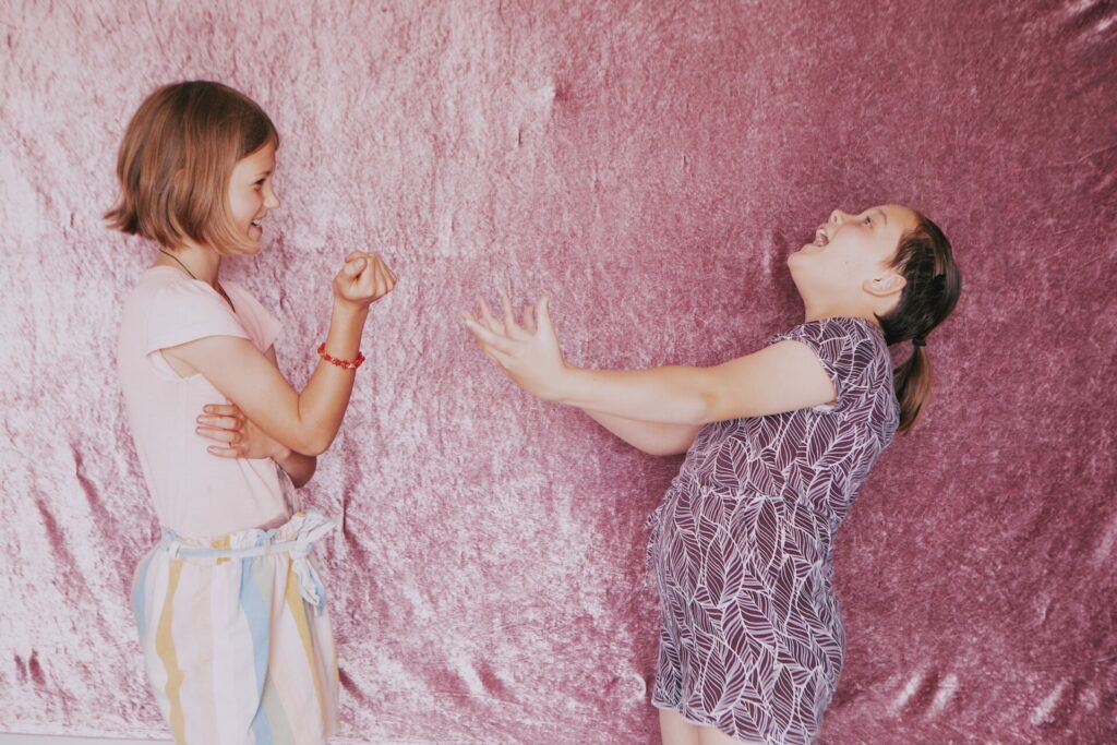 Two girls stand in front of pink velvet making gestures