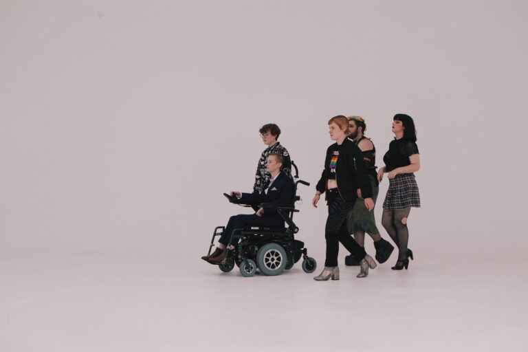 Five young people, one in a wheelchair, cross a white studio