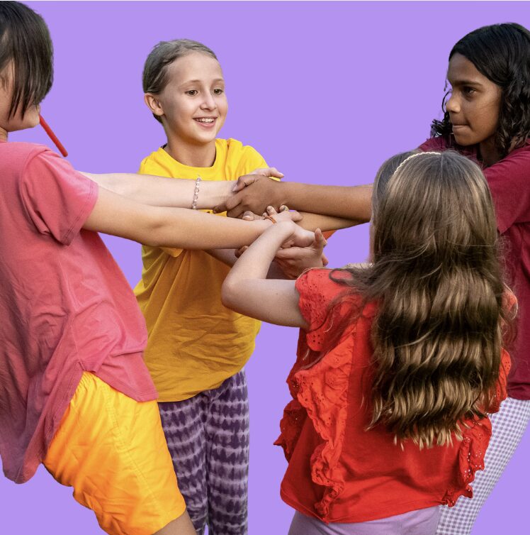 4 young girls in coloured t-shirts form a circle on a purple background. They are holding each other's arms in the centre. (From Gene Tree Darwin performance)
